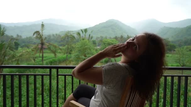 Mooie vrouw zit aan appartement balkon met prachtig uitzicht op de bergen waait kus voor camera, het verzenden van groeten van tropische plaats genieten van haar vakantie, inspirerende positieve houding — Stockvideo