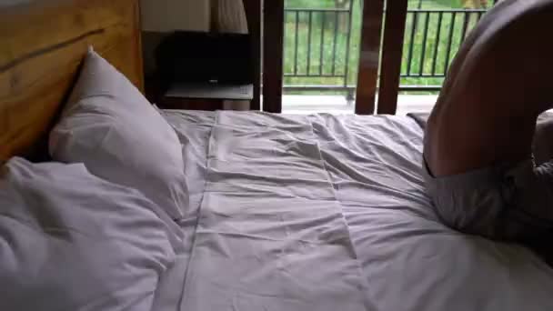 Χαρούμενος νεαρός πέφτουν στο κρεβάτι σε δωμάτιο ξενοδοχείου, χαλαρώνοντας στην ιδέα του Ενοικιαζόμενα — Αρχείο Βίντεο