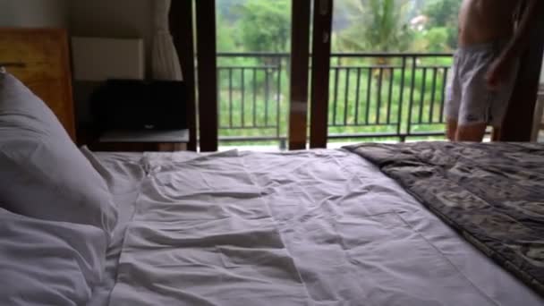 Χαρούμενος νεαρός πέφτουν στο κρεβάτι σε δωμάτιο ξενοδοχείου, χαλαρώνοντας στην ιδέα του Ενοικιαζόμενα — Αρχείο Βίντεο