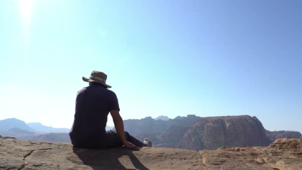 Hombre senderismo viajero sentado en el borde de las montañas y mirando a su alrededor en el paisaje hermoso — Vídeos de Stock