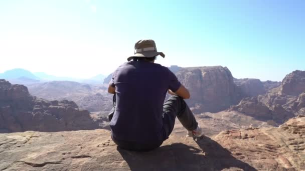 Uomo seduto in cima alla montagna e guardando splendida vista, vetta della petra antica città in — Video Stock