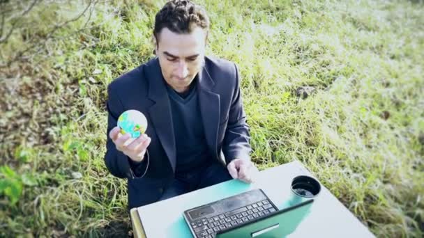 Mladý atraktivní podnikatel v obleku s notebookem sedícím venku na zelené louce, kancelář — Stock video