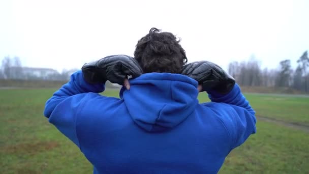 Concetto di solitudine, uomo solo in piedi all'aperto nel parco, vista posteriore, indossando guanti da boxe, lotta — Video Stock