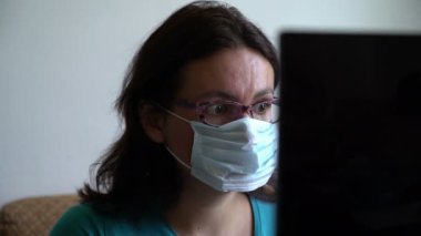 Maskeli ve gözlüklü kadın, dizüstü bilgisayarında virüs pandemisi hakkında yeni şeyler okuyor, korkmuş ve şok olmuş görünüyor.