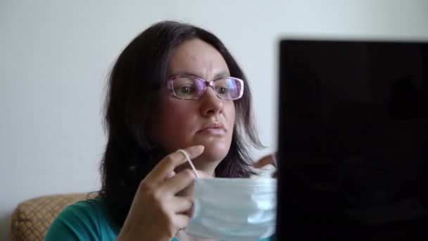 Женщина надевает маску, читает новое о пандемии вируса на ноутбуке, выглядит испуганно и — стоковое видео