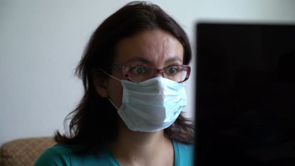 Frau setzt Maske auf, liest Neues über Virenpandemie auf Laptop, sieht erschrocken aus und — Stockvideo