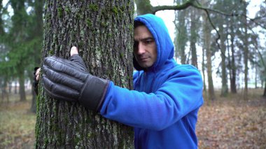Boks eldivenli genç adam ormanda ağaca sarılıyor ve doğayı seviyor. Yetişkin Kafkas 'ın elleri