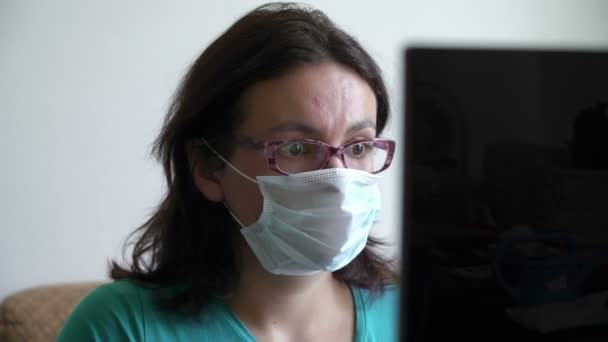 Mujer estresante sentada en máscara cerca del portátil y leyendo nuevo, puesto de gafas. Cuarentena domiciliaria, social — Vídeos de Stock