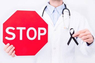 Onkolojik hastalık konsepti. Doktor beyaz önlük ve steteskop takıyor. Elinde melanom kanserinin sembolü olarak siyah kurdele ve dur işareti var.