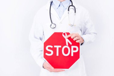 Onkolojik hastalık konsepti. Beyaz önlük giyen ve steteskop tutan bir doktor tarafından izole edilmiş arka planda göğüs kanserinin sembolü olarak pembe kurdele kullanılıyor.