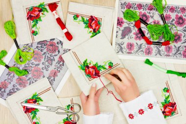 Ukraynalı geleneksel tişörtlü, nakış işlemeli kadın / kız elleri. Arkaplanda nakış şeması ve renkli iplikler.