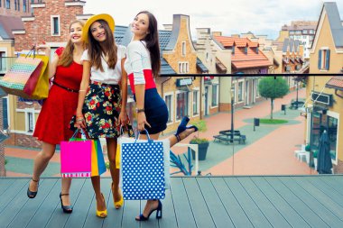 Oldukça mutlu, renkli elbiseli ve yüksek topuklu ayakkabı giyen, alışveriş merkezlerinde sıcak yaz mevsiminde alışveriş yaptıktan sonra alışveriş torbalarıyla sokakta yürüyen yetişkin kadın kadınlar. Mağaza satışları, Kara Cuma turist konsepti.