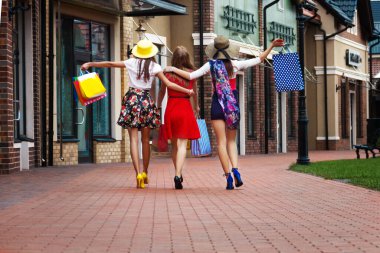 Renkli elbiseler, şapkalar ve yüksek topuklu ayakkabılar içinde alışveriş merkezlerinde alışveriş yaptıktan sonra sokakta yürüyen oldukça mutlu, zeki bayan kızlar. Mağaza satışları, Kara Cuma.