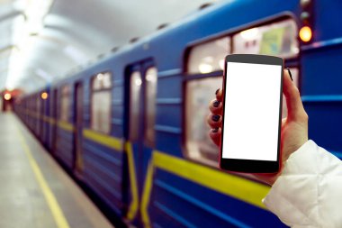 Kışın arka planda metro ve toplu taşıma istasyonları olan akıllı telefon / cep telefonlu kadın / kadın eli