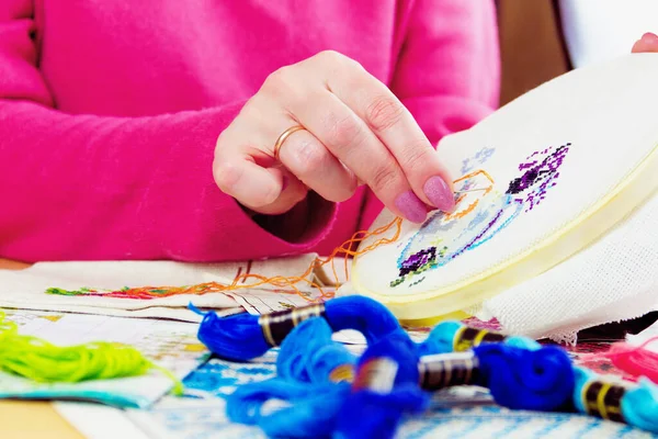 Beyaz tuval üzerinde çiçekli kadın eli işlemeli vazo. Renkli iplikleri ve resimleri olan çalışma yeri 