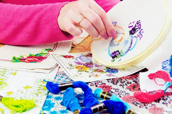 Beyaz tuval üzerinde çiçekli kadın eli işlemeli vazo. Renkli iplikleri ve resimleri olan çalışma yeri 