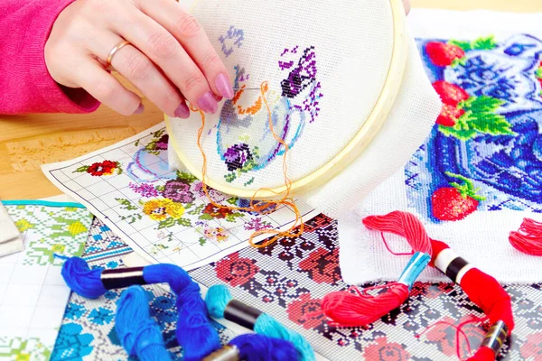 Beyaz tuval üzerinde çiçekli kadın eli işlemeli vazo. Renkli iplikleri ve resimleri olan çalışma yeri 