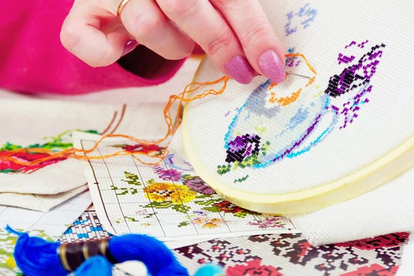 Beyaz tuval üzerinde çiçekli kadın eli işlemeli vazo. Renkli iplikleri ve resimleri olan çalışma yeri 