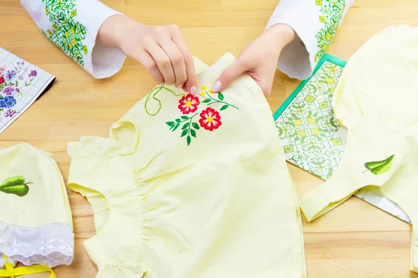 Geleneksel Ukrayna tişörtlü kadın / kız çocuklarının çiçek desenli elbiselerini dikiyor. Terzi işyeri: nakış işleri ve tahta arka planda çocuk elbiseleri