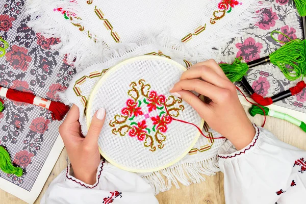 Ukraynalı geleneksel tişörtlü, nakış desenli nakış nakışlı kadın / kız elleri. Arkaplanda nakış şeması ve renkli iplikler.