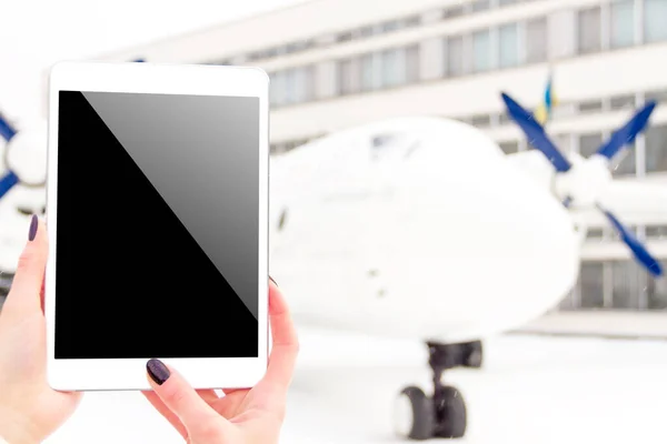 Mockup white tablet in woman / female / girl hand with airplane and fir tree on background in winter