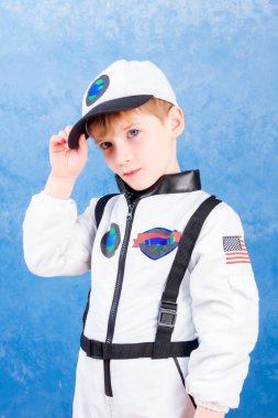 Beyaz astronot kostümüyle astronotluk yapan ve mavi arka planda kozmosa uçtuğunu hayal eden genç çocuk.