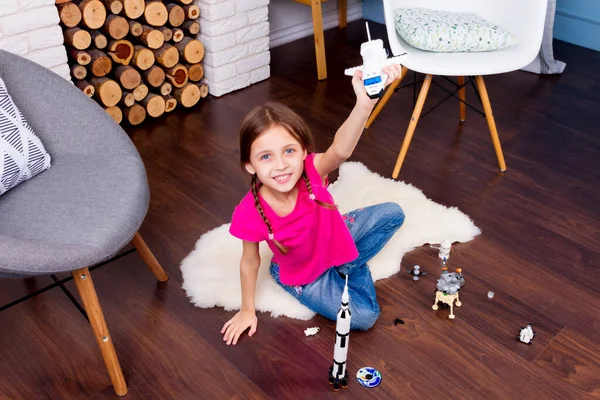 Young child girl female playing with cosmos\'s toys constructor: rocket, shuttle, rover, satellite and astronaut doll in comfortable interior at home on wooden floor
