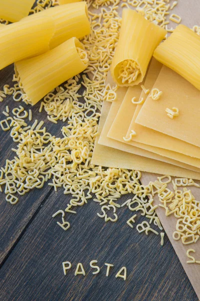 Uncooked raw pasta alphabet yellow letters with macaroni and lasagna — Stock Photo, Image