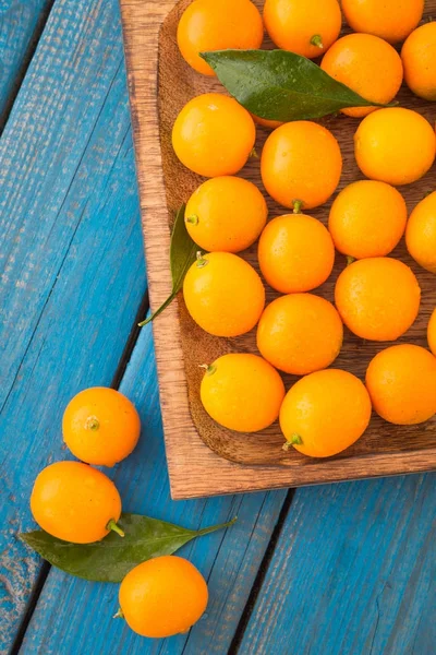 Assiette en bois de cumquats frais mûrs ou de kumquats aux feuilles vertes — Photo