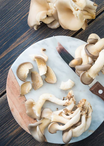 Cogumelos de ostra frescos que cortam na placa de corte de mármore — Fotografia de Stock