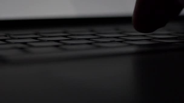 Macro lateral cerca de mano masculina mecanografía en habitación oscura con teclado retroiluminado portátil . — Vídeos de Stock