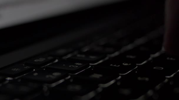 Lado Primer plano mano masculina escribiendo en habitación oscura con teclado retroiluminado portátil . — Vídeo de stock