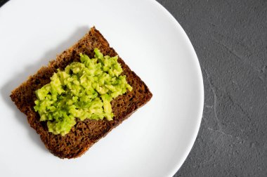 Avokado ve tahıllı ekmeği ezip, tabakta ve beton manzaralı bir tost.