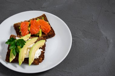Avokado dilimli, krem peynirli iki tost ve beyaz tabakta kırmızı balık somonlu avokado ezmek ve beton.