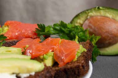 Kırmızı balıklı tost ve maydanozlu avokado püresi ve arka planda avokado dilimi.