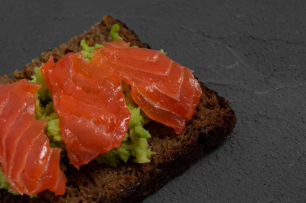 Closeup multi-cereal bread toast with smash avocado and red fish salmon on concrete