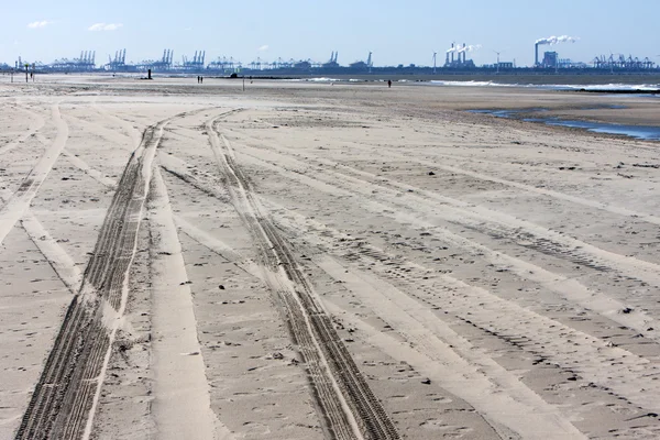 Tire tracks on the beach and Rotterdam industry in background — Stockfoto