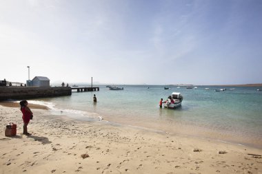Buralı bir kadın, geleneksel bir balığın yakınındaki iki adamı izliyor.