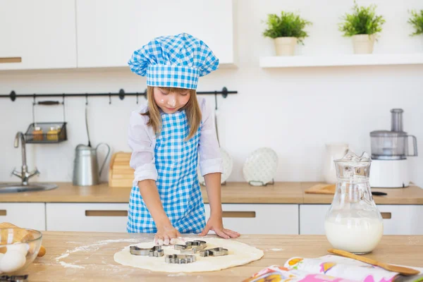 La ragazza carina in vestiti di cuoco spinge da una scatola di torta su una pasta su un tavolo — Foto Stock