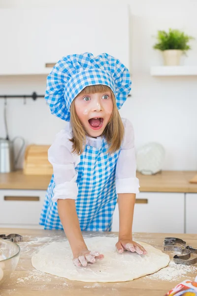 Bella bambina in abiti da cuoco scolpisce un impasto e aprire gli occhi e la bocca su una cucina — Foto Stock