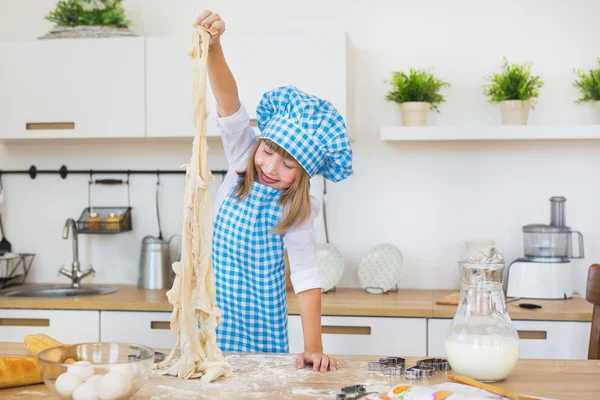 La bambina in un cuoco gioca con una pasta su un tavolo e sorride — Foto Stock