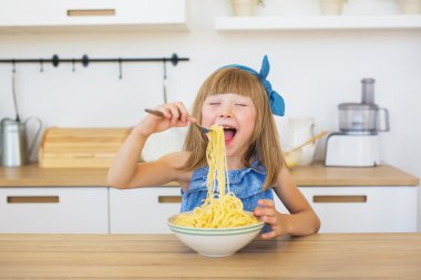 Mavi elbiseli gülümseyen bir küçük kız portresi, komik bir spagetti yiyen