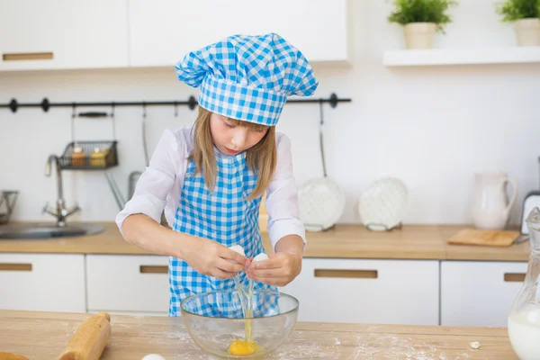 La bambina in vestiti di cuoco rompe un uovo in una boccia su un tavolo — Foto Stock