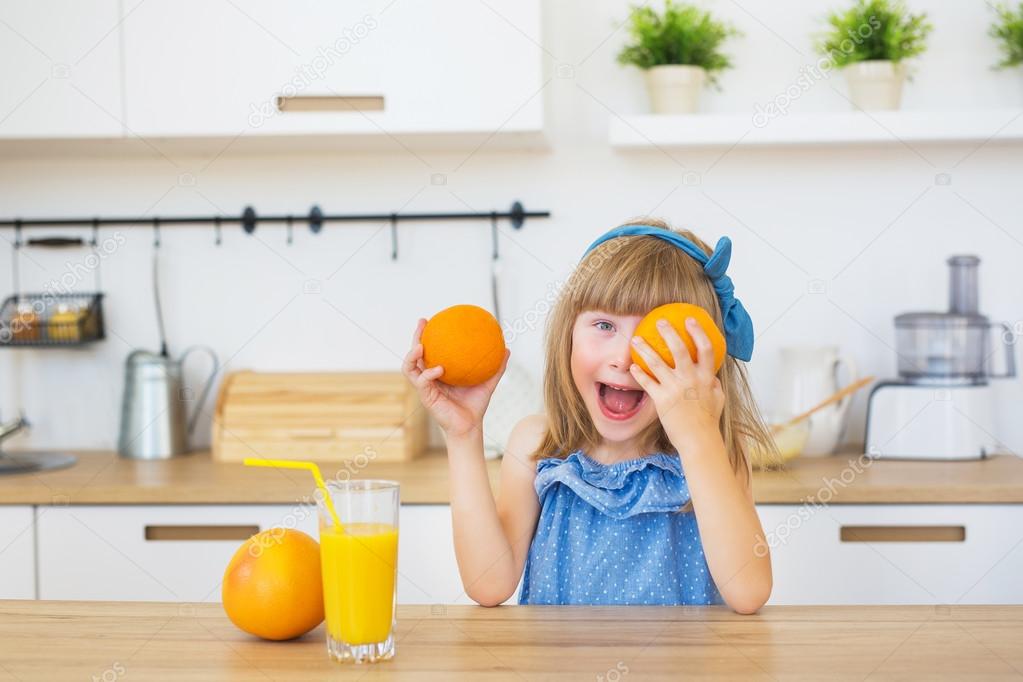 Portrait of a little girl in a blue dress plays with an oranges on a table
