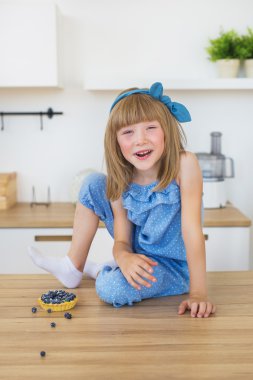 Sevimli küçük kız mavi elbiseli bir masaya oturur ve gülümser ve