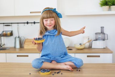 Sevimli küçük kız mavi elbiseli bir el ve kapalı gözler pastada bir masada oturur
