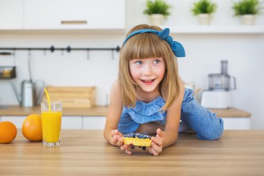 Sevimli küçük kız mavi elbiseli bir masaya oturur ve bir çerez yemek istiyorum