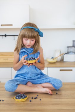 Sevimli küçük kız mavi elbiseli bir pasta bir masada oturur ve üzerinde görünüyor
