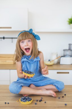Sevimli küçük kız mavi elbiseli bir pasta bir masada oturur ve ağzını açın