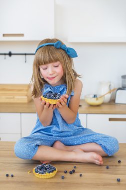 Sevimli küçük kız mavi elbiseli bir pasta bir masada oturur ve üzerinde görünüyor ve dudaklarını yalıyor
